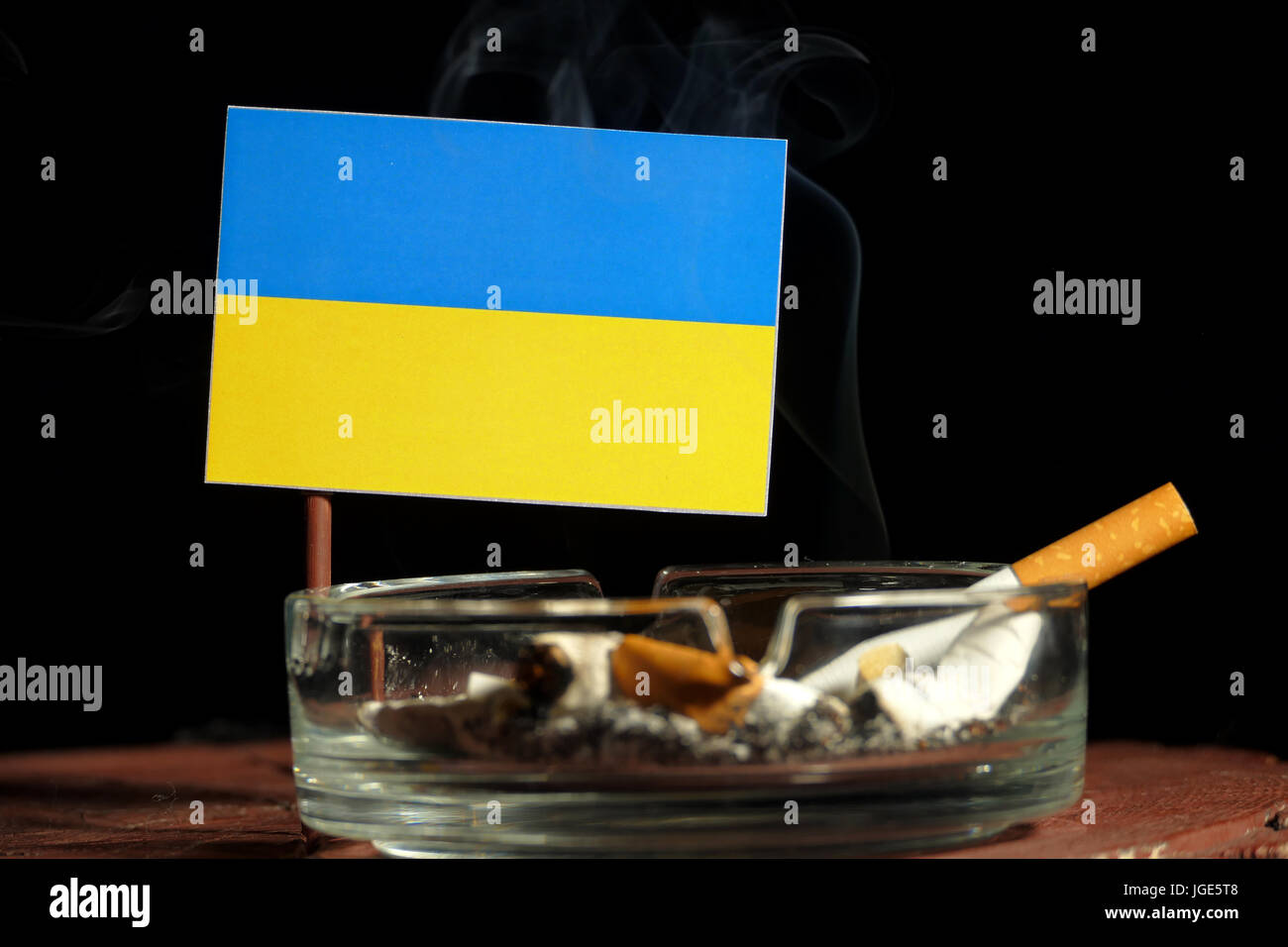 Ukraine flag with burning cigarette in ashtray isolated on black background  Stock Photo