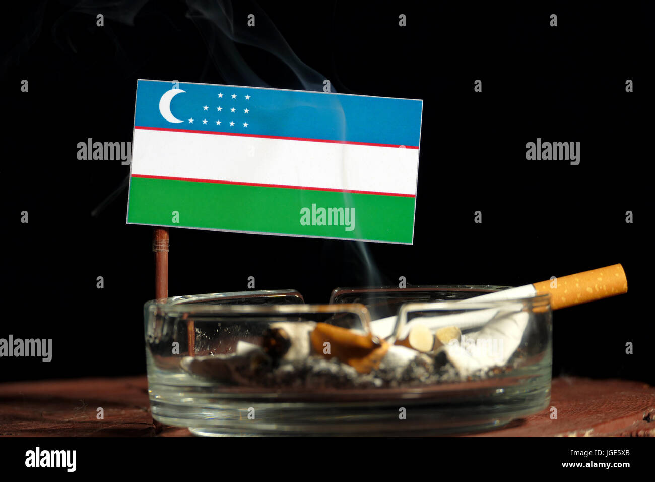 Uzbekistan flag with burning cigarette in ashtray isolated on black  background Stock Photo