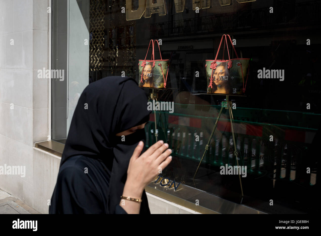 A Muslim lady wearing a Niqab passes the luxury shop window of Louis Vuitton  featuring their exclusive range of bags with the face of Leonardo da  Vinci's Mona Lisa - a collaboration