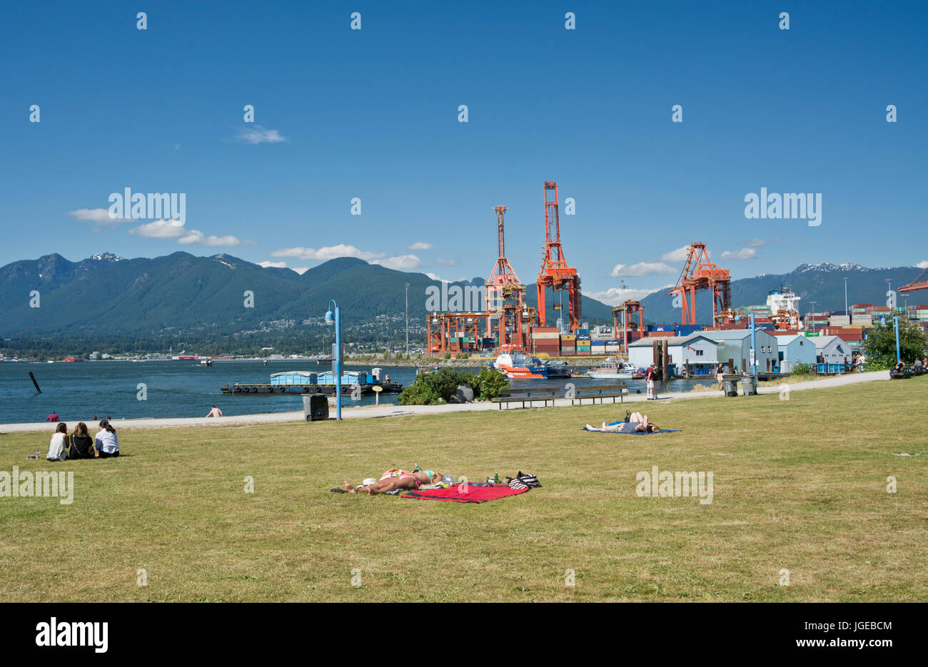 Crab Park in Vancouver BC- people sunbathing and enjoying the water views.  Loading docks at Port of Vancouver. Stock Photo