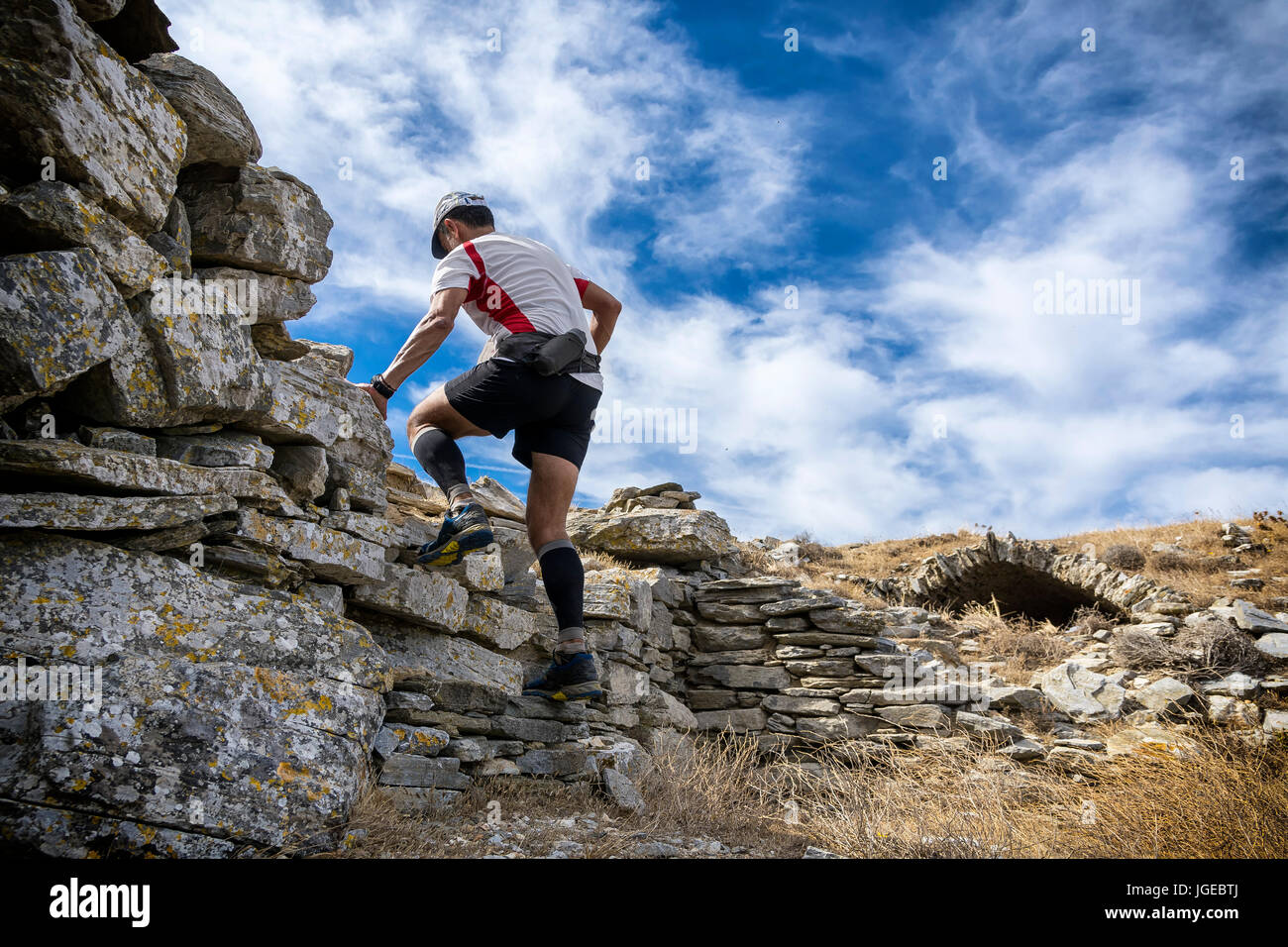 trail runner climbing a rocky hill with ancient monument Stock Photo