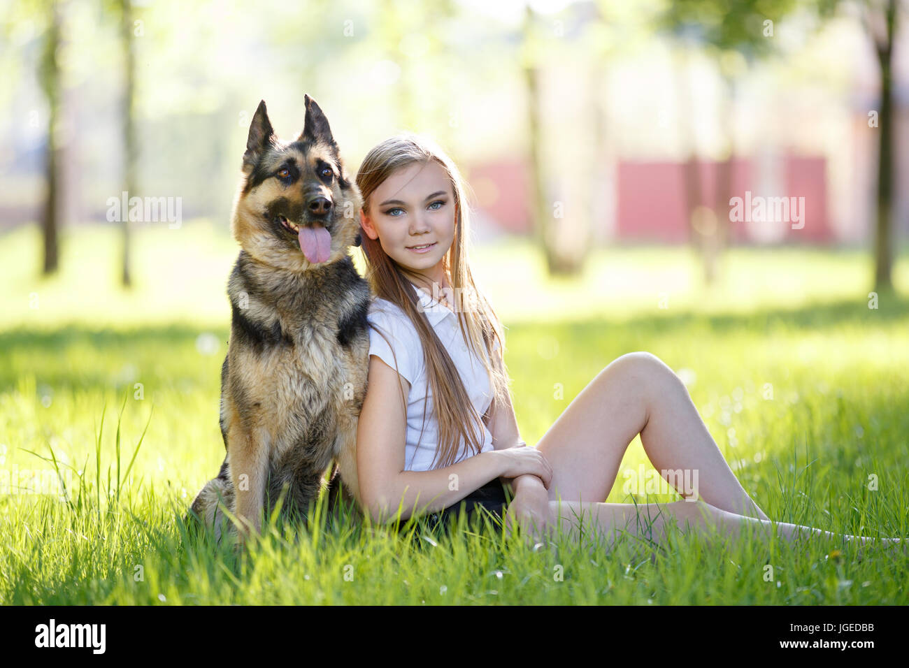 Teenage girl in white shirt with her dog sitting on grass in the park ...