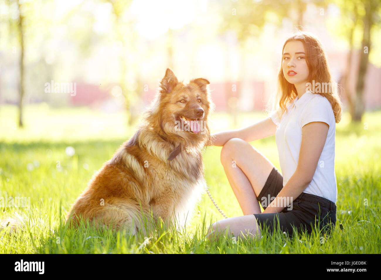 Teenage smiling girl in white shirt with her dog sitting on green grass ...