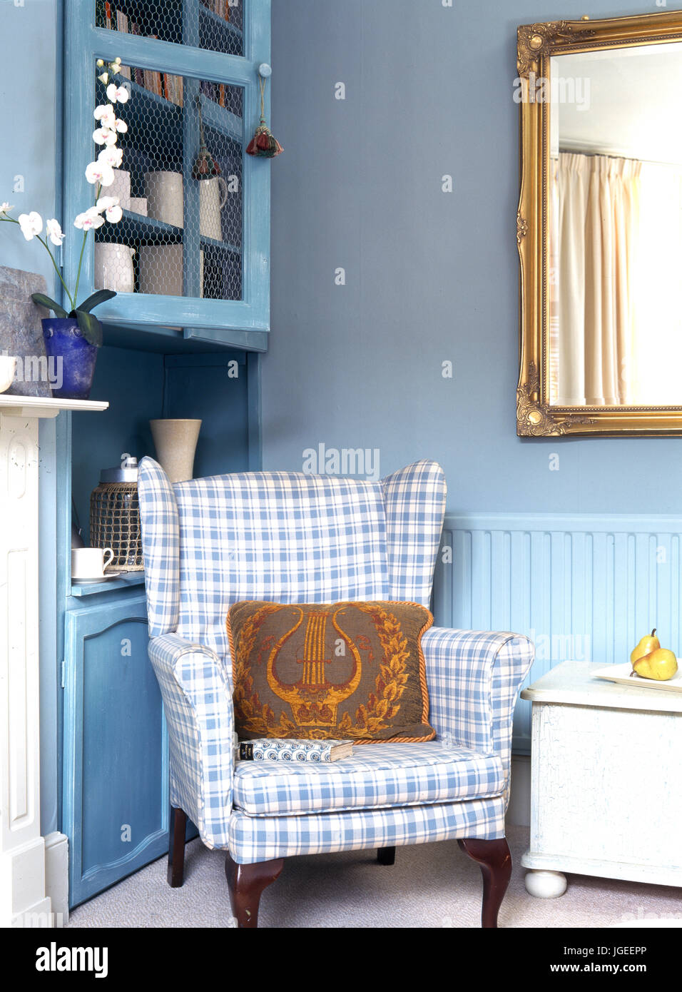 Blue and white checked pholstered wing chair in corner of room Stock