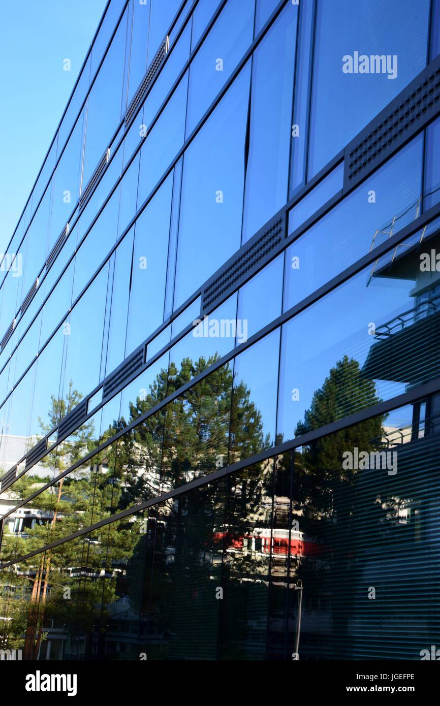 trees reflected in windows of modern building, glass facade with ...