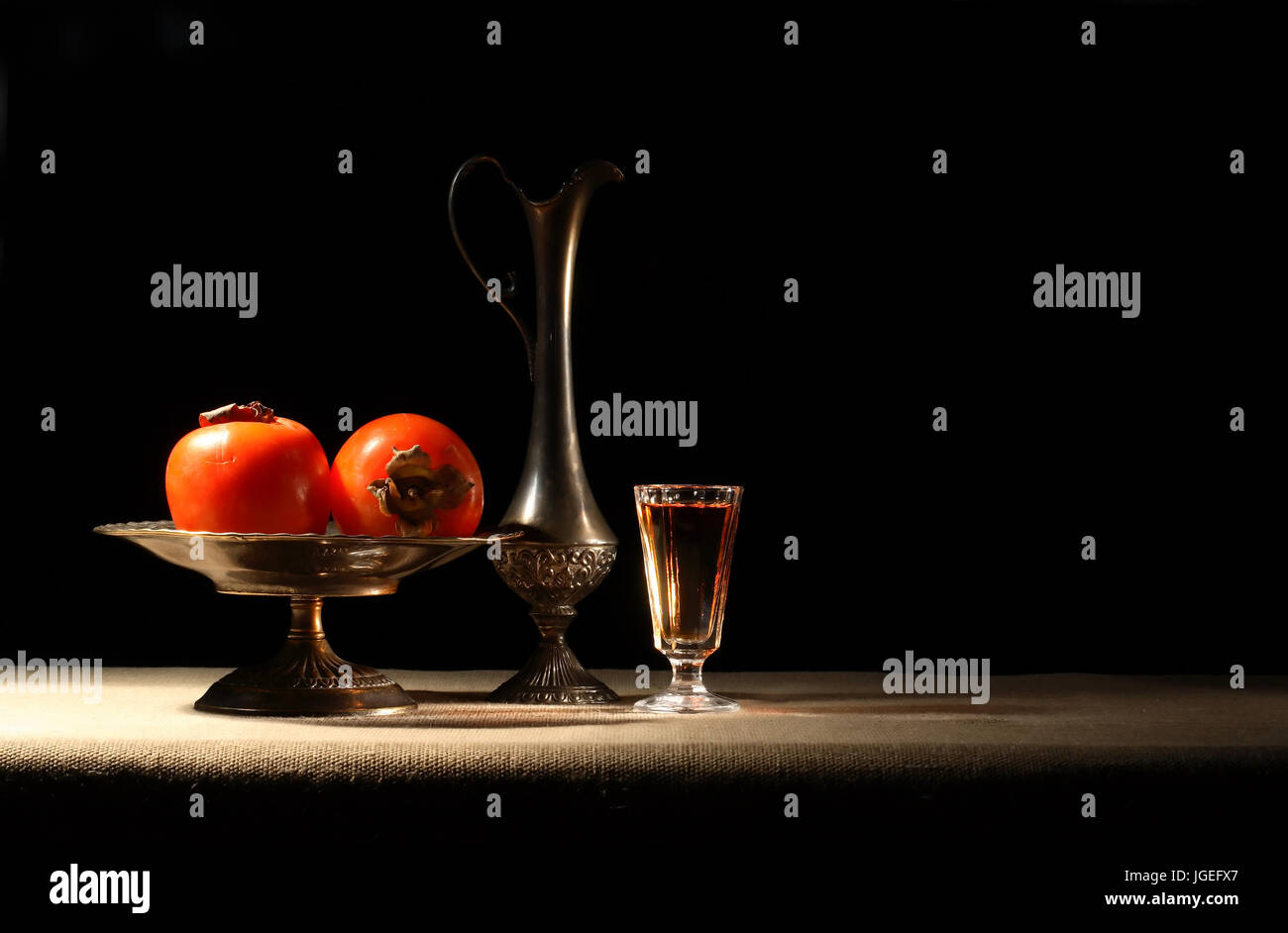 Antique vases with persommons near glass of wine on dark background Stock Photo