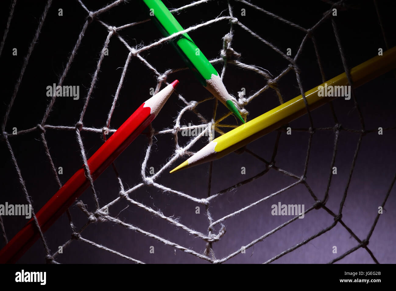 Web design concept. Three color pencils in rope web on dark background Stock Photo