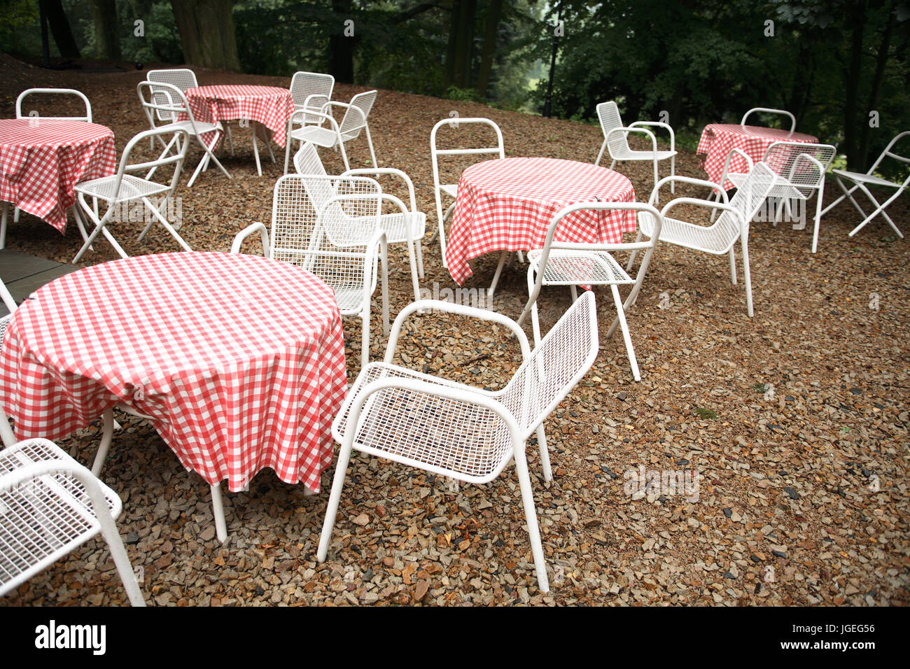 Few empty restaurant tables and chairs between trees Stock Photo
