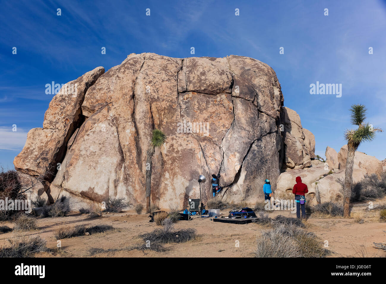 Several rock climbing friends stand around below a large stone climbing challenge Stock Photo