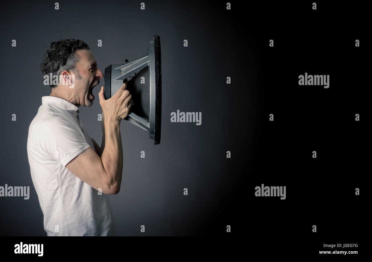 Young man holding a big speaker, speaking loud concept on a dark studio