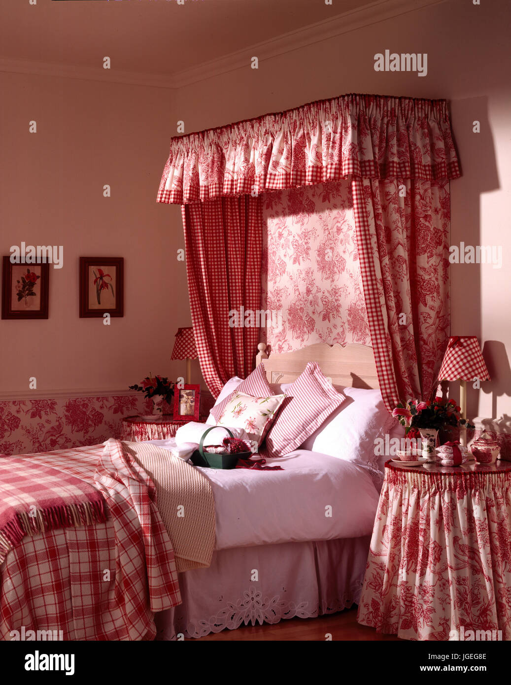 Double bed with deep pink fabric bed hangings to match print on wall below dado. Stock Photo