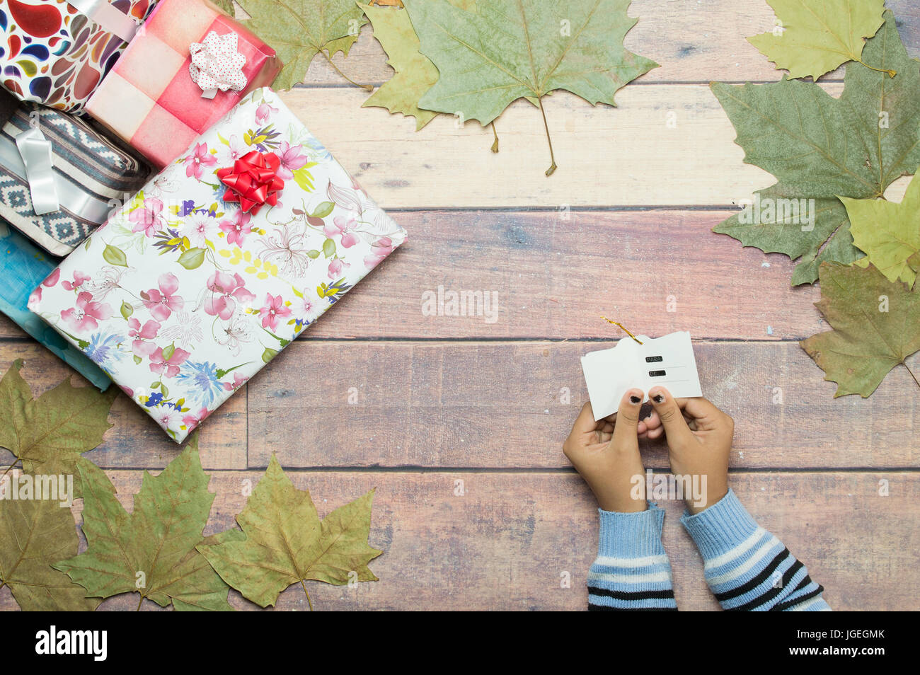 hands of girl opening gift card on wooden table with autumn leaves Stock Photo