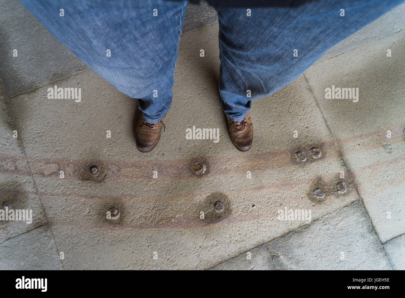 Man's legs and leather boots standing on empty ground with rusted rails embedded in stone Stock Photo