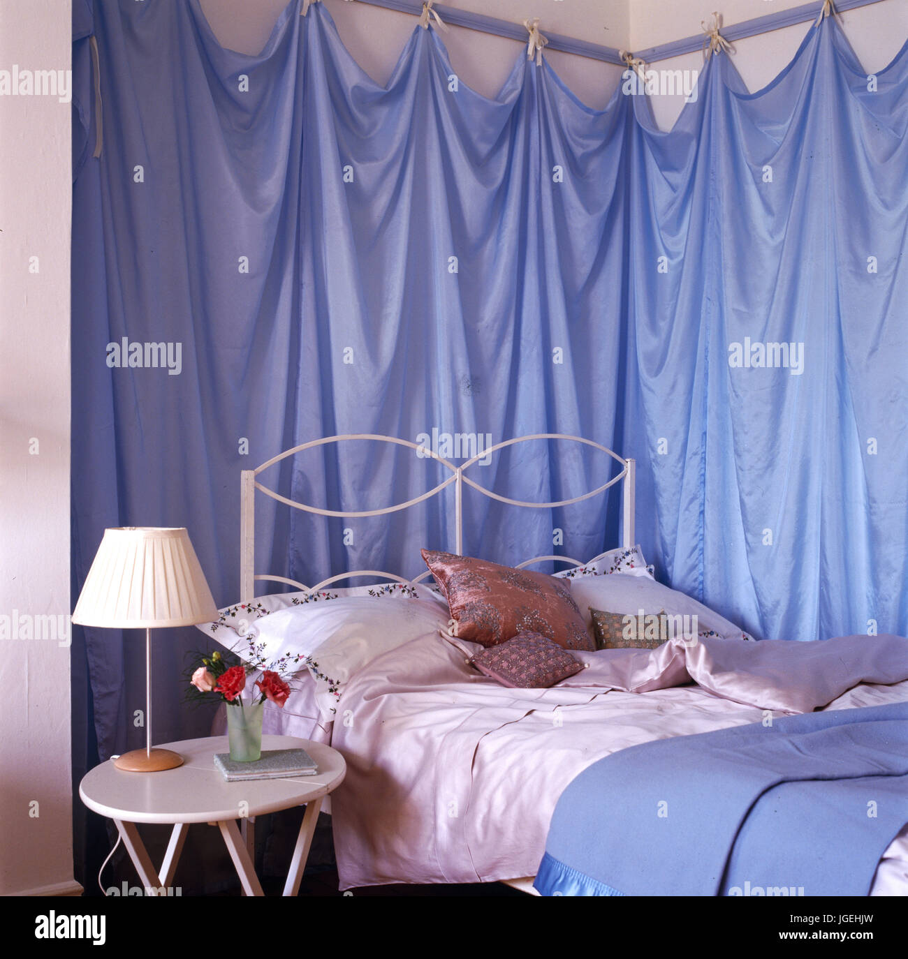 Corner Of Bedroom With Blue Fabric Drapes On Walls Above Bed Stock