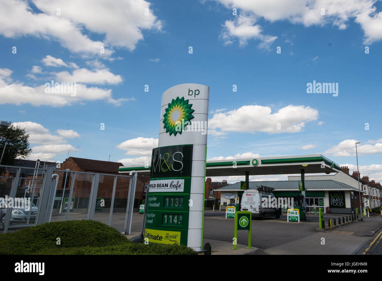 BP petrol Station Northampton England sign signs fuel  clouds blue sky cost van filling up M@S food BP green petrol diesel shop shopping arrow fence Stock Photo