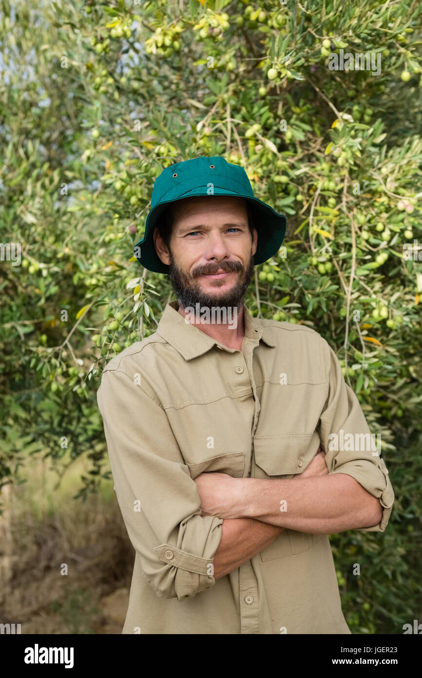 Portrait of smiling farmer standing with arms crossed in olive farm ...