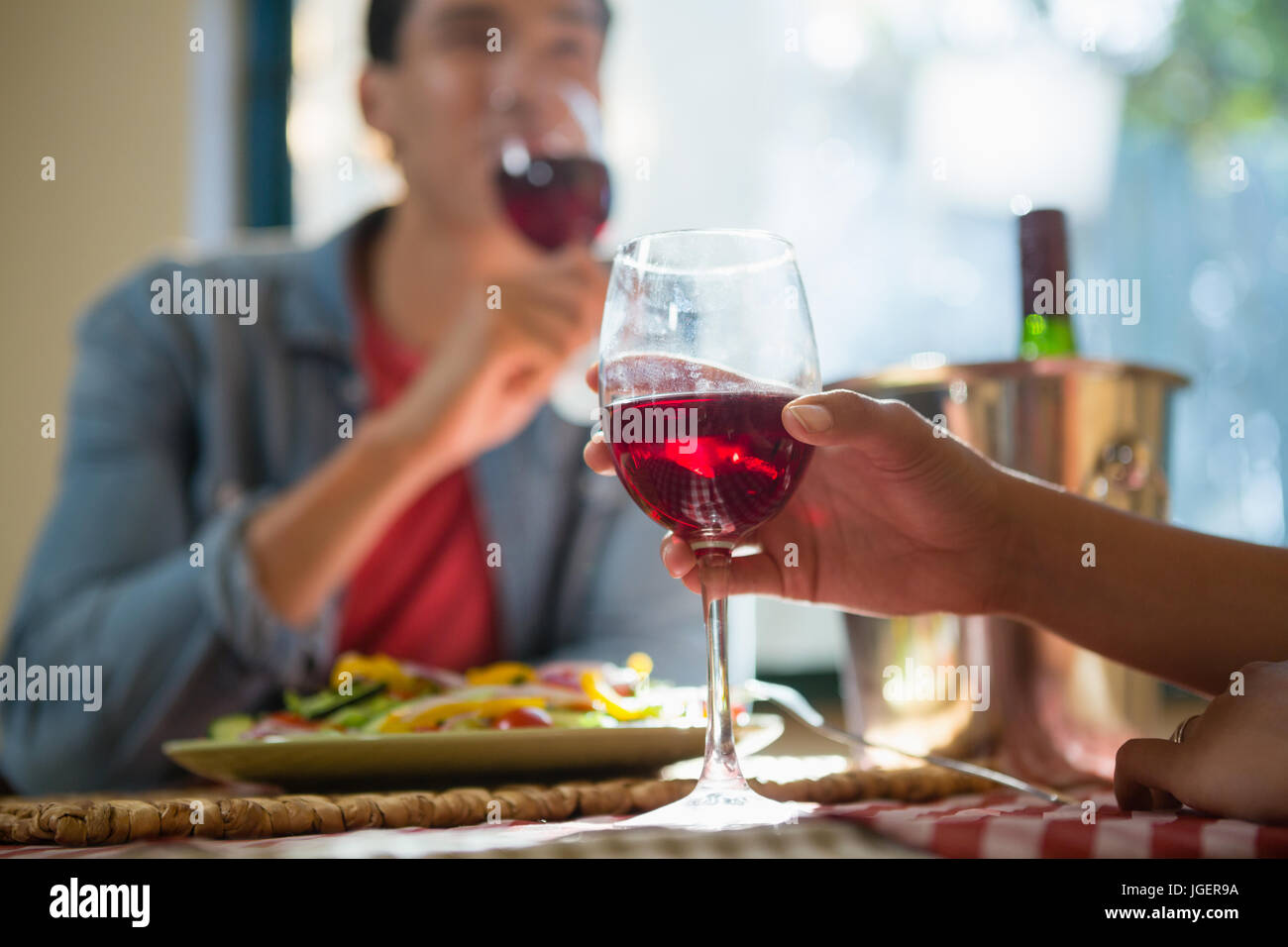 Cropped hand of woman with friend holding wineglass at table in restaurant Stock Photo