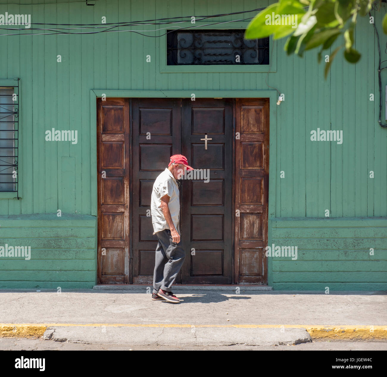 Old Man Walks By A Front Door Of A House With A Cross In Corinto Nicaragua Stock Photo