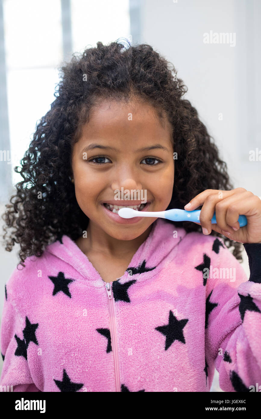Portrait of smiling girl brushing her teeth in bathroom at home Stock Photo