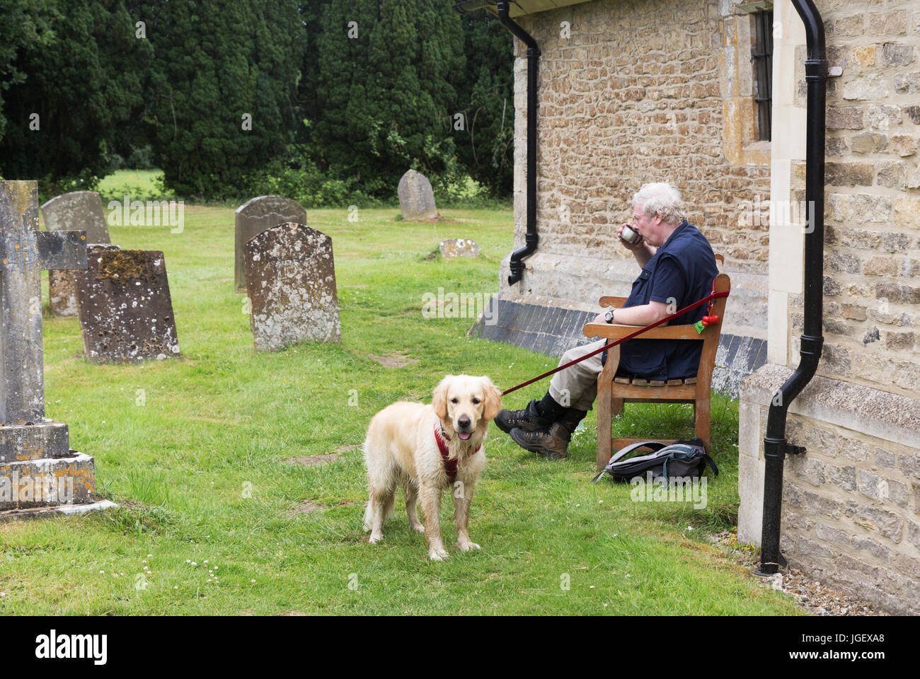 Dog walker - a senior man sitting down for a rest in a churchyard while walking the dog, Appleton, Oxfordshire UK Stock Photo