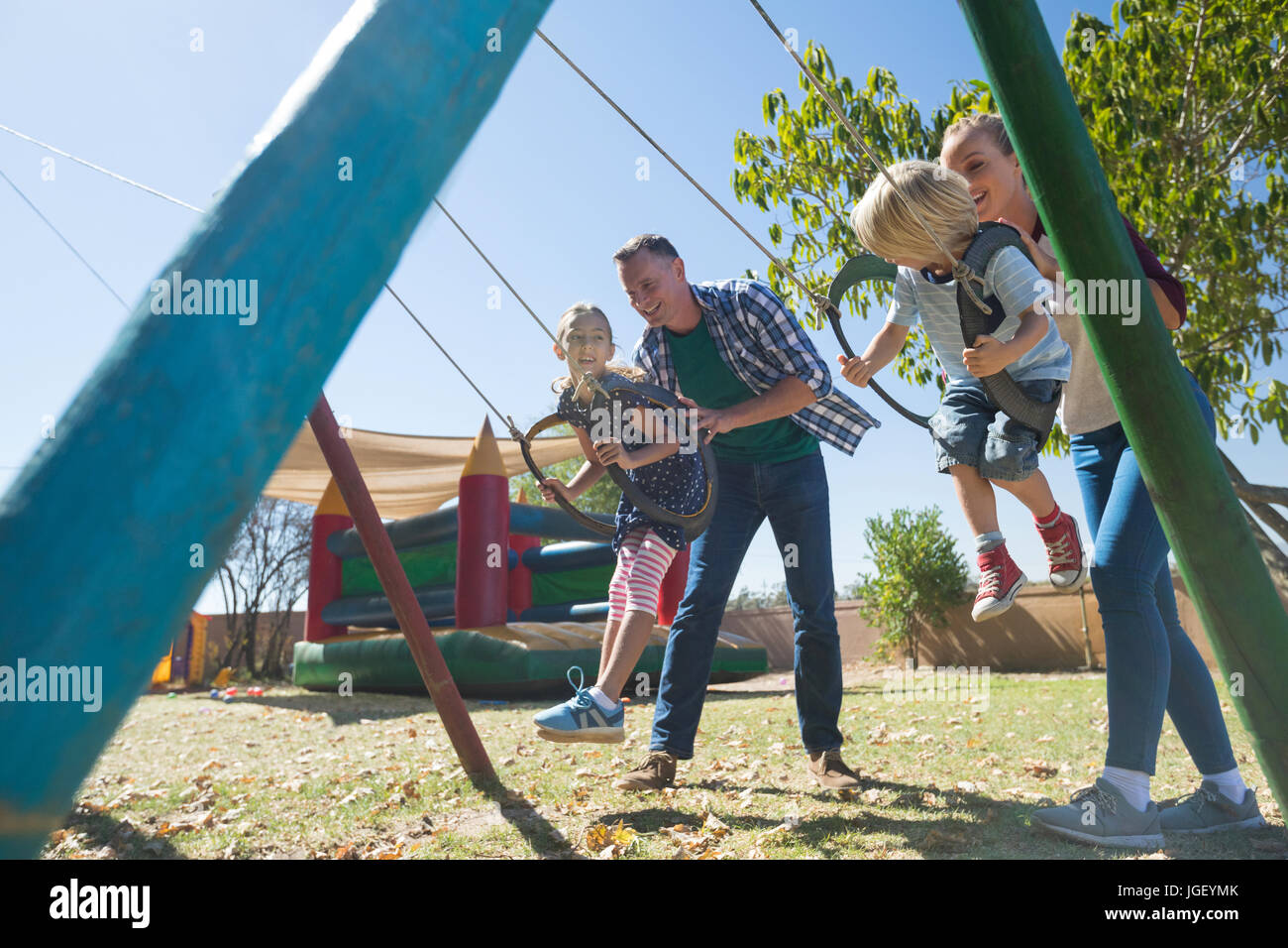 Playful parents swinging children at playground during sunny day Stock Photo