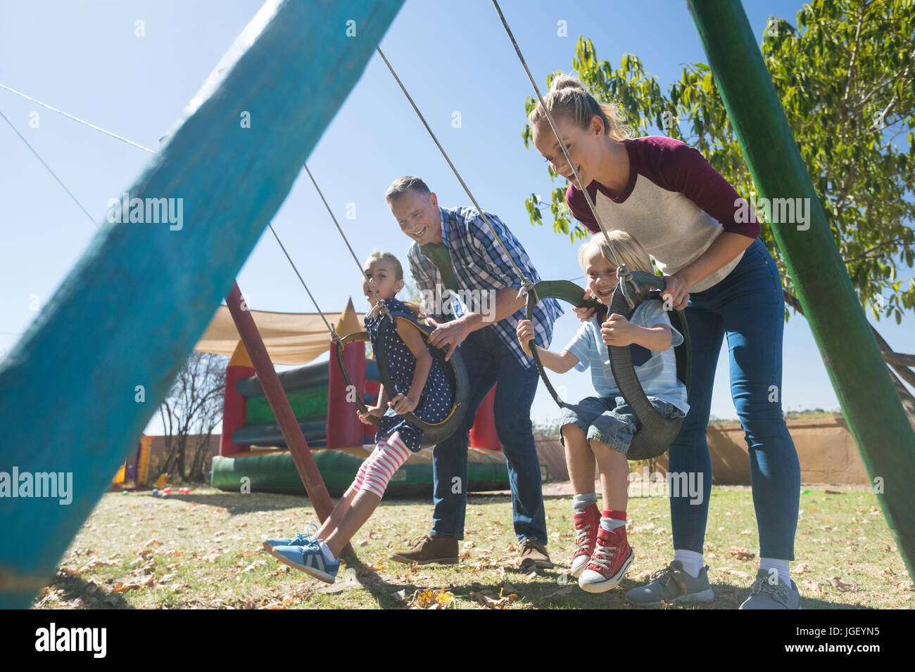 Happy parents swinging children at playground during sunny day Stock Photo