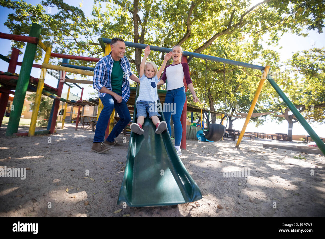 Low angle view of happy parents looking at son sliding at playground Stock Photo