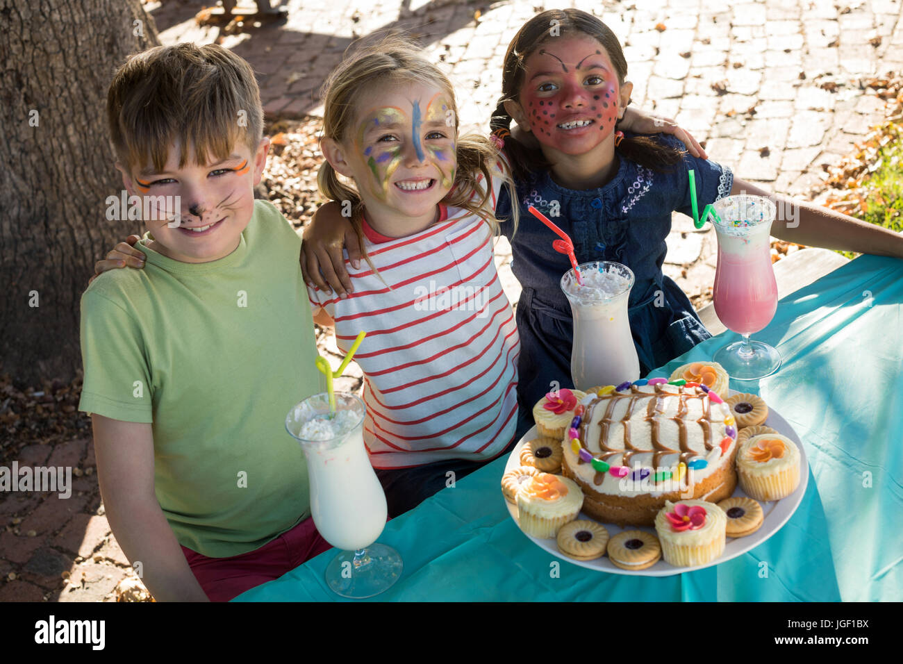 Portrait of happy friends with face paint sitting by food and drink at table Stock Photo