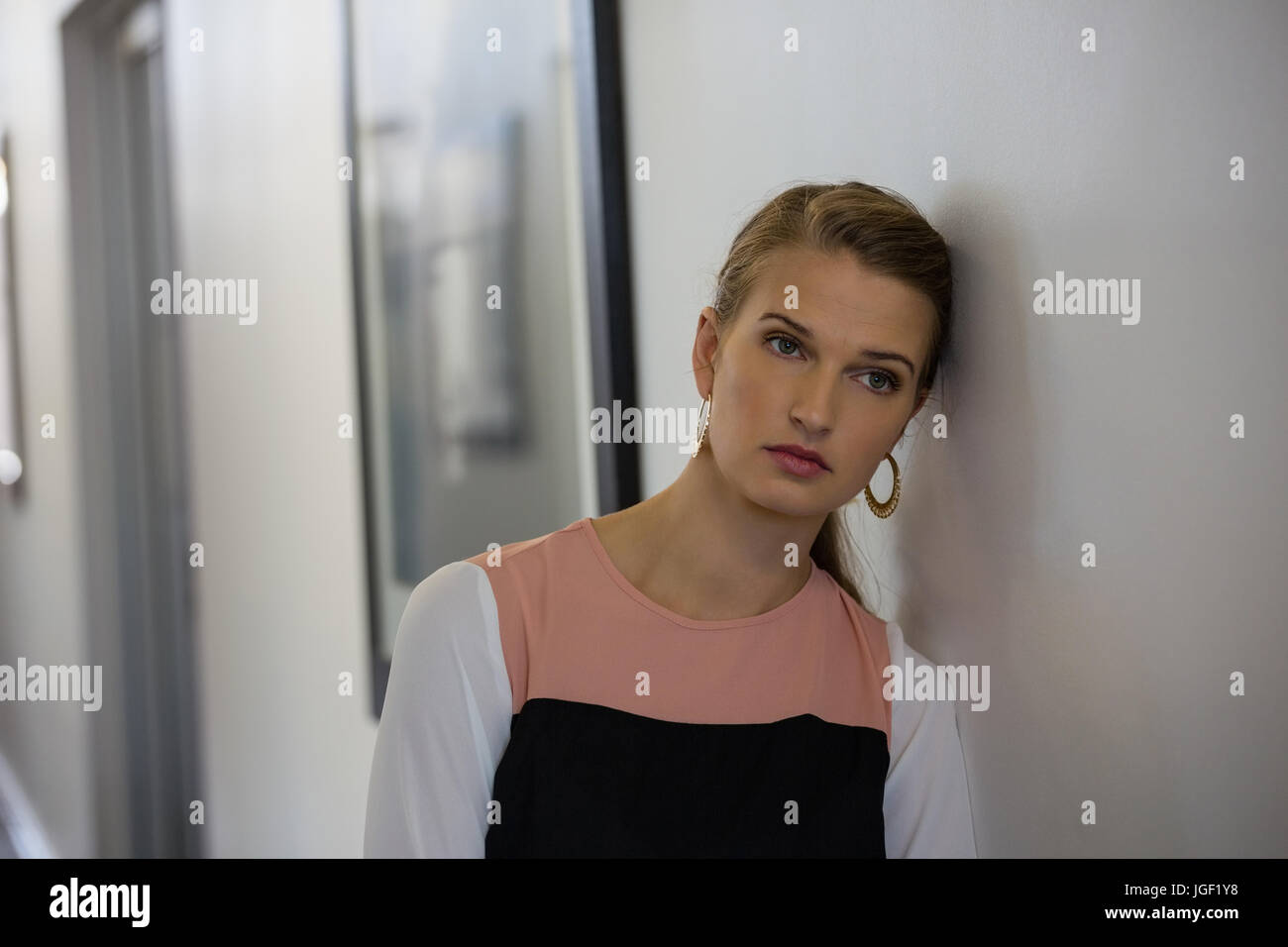 Sad businesswoman looking away while leaning on wall at office Stock Photo