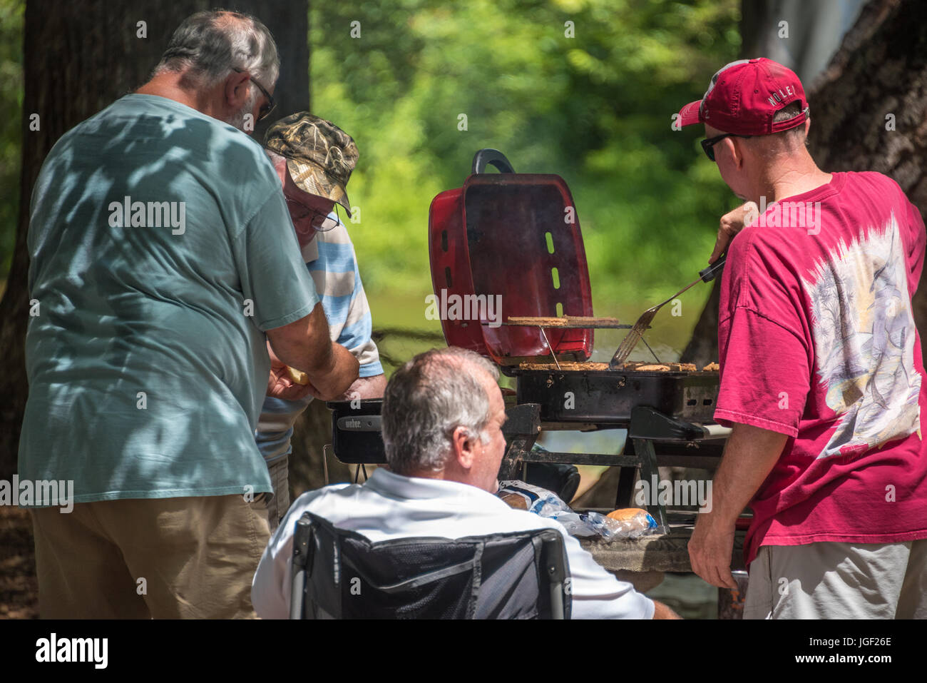 Men grilling burgers and hot dogs for a family gathering along the Chattahoochee River in Helen, Georgia. (USA) Stock Photo