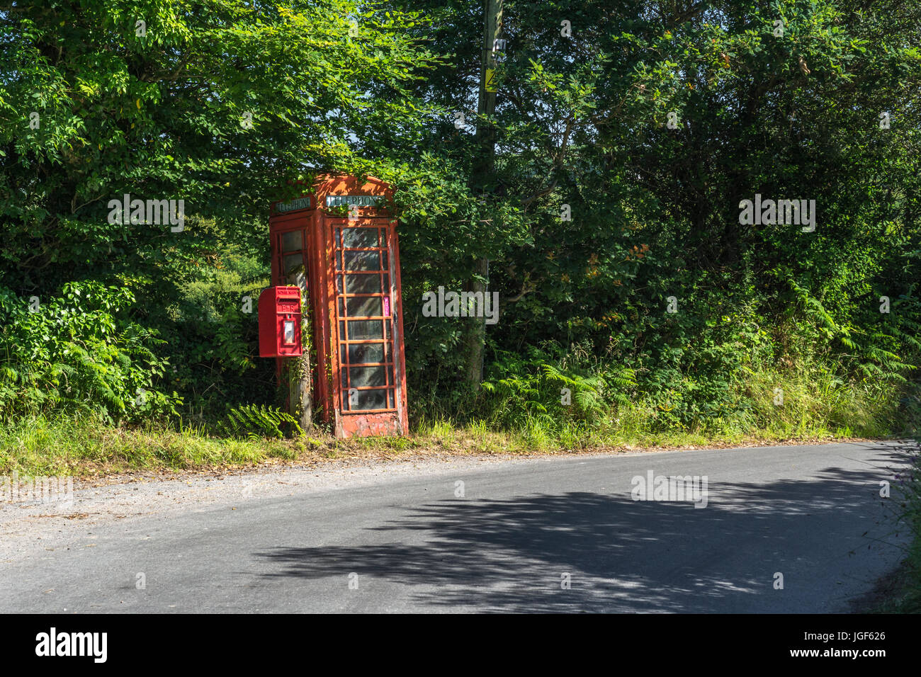 Old red telephone box and red letter posting box on country / rural road in Cornwall, UK. Box and telegraph pole to right angled because of subsidence Stock Photo