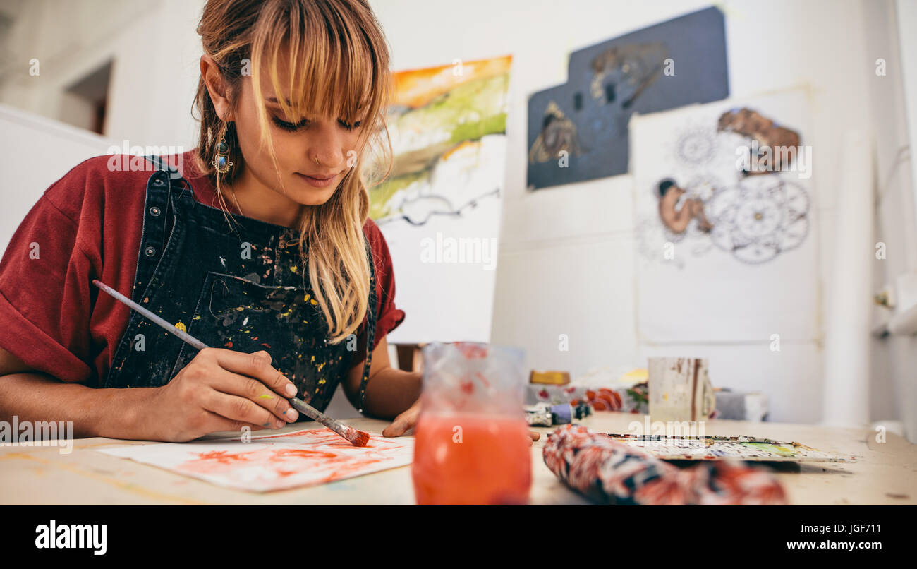 Shot of beautiful young female artist painting in studio. Woman painter drawing on paper in her workshop. Stock Photo