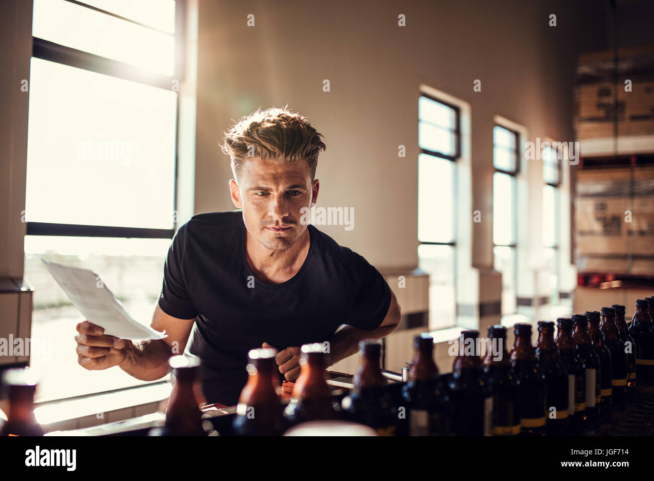 Brewery factory worker examining the quality of craft beer. Young man inspector working on alcohol manufacturing factory checking the beer bottles. Stock Photo