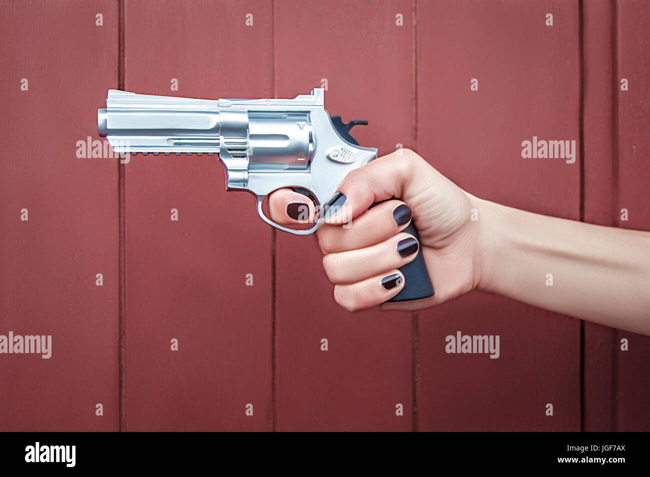 Woman hand with nail polish, holding a gun on a red background Stock