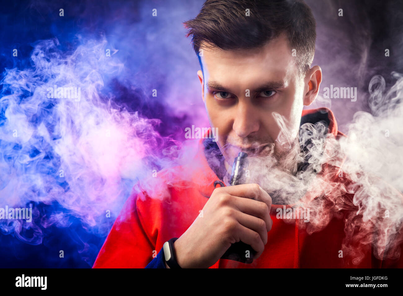 A man smokes a vape, lets steam, studio, colored smoke Stock Photo