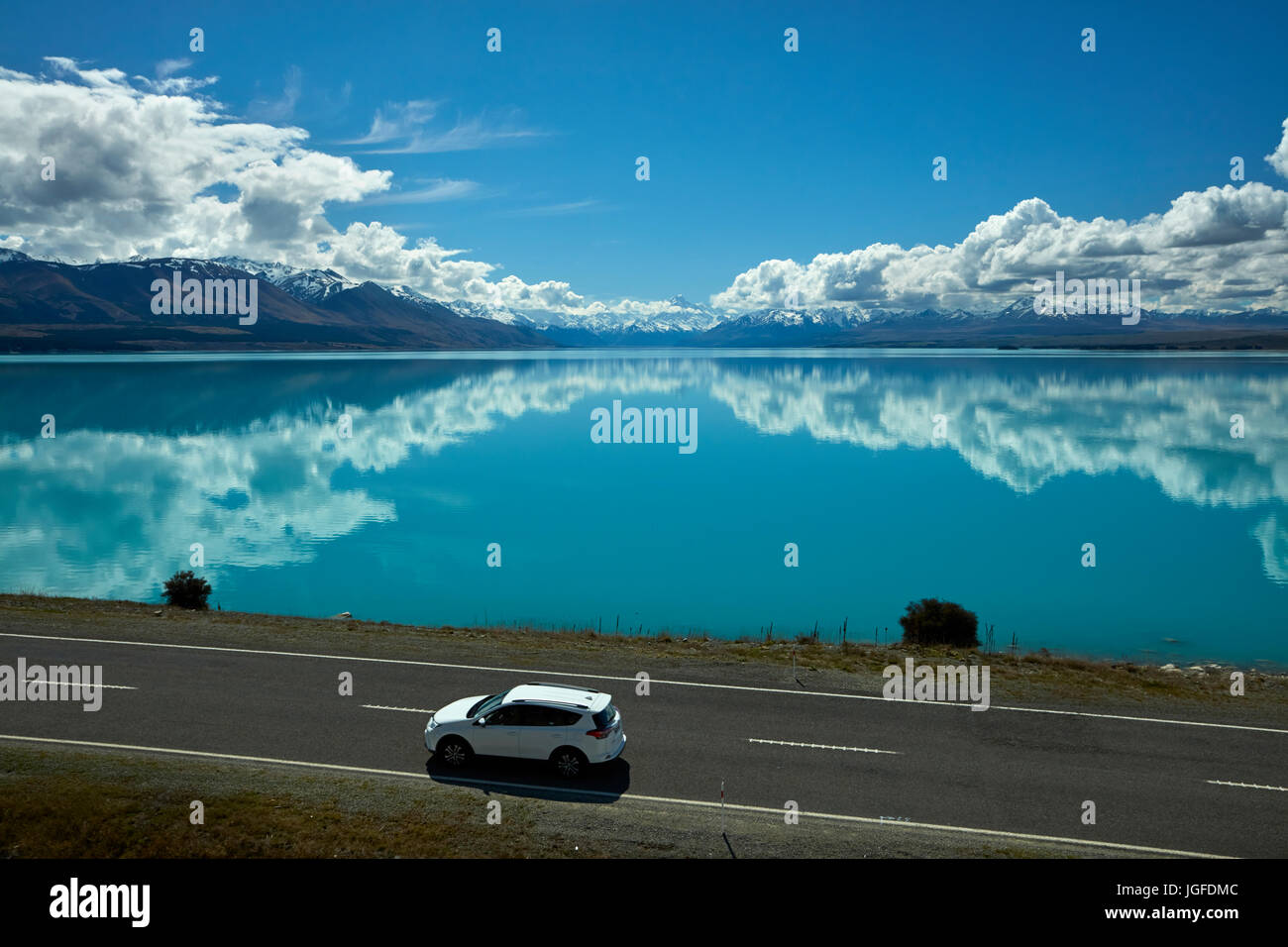SUV on State Highway 8, and Aoraki / Mount Cook reflected in Lake Pukaki, Mackenzie Country, Canterbury, South Island, New Zealand Stock Photo