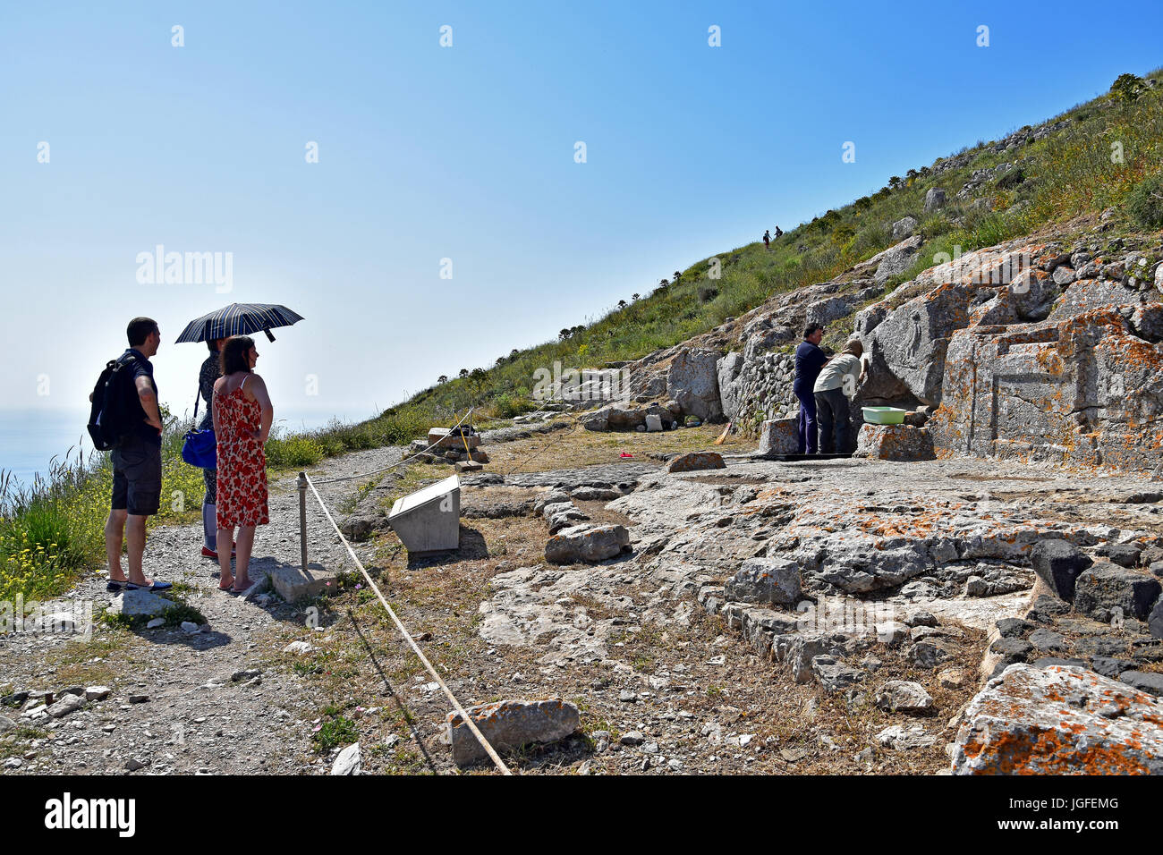 Tourists watching greeks restoring carvings on the remains of Ancient Thira, Sanctuary of Artemidoros Kamari, Santorini, Greece Stock Photo