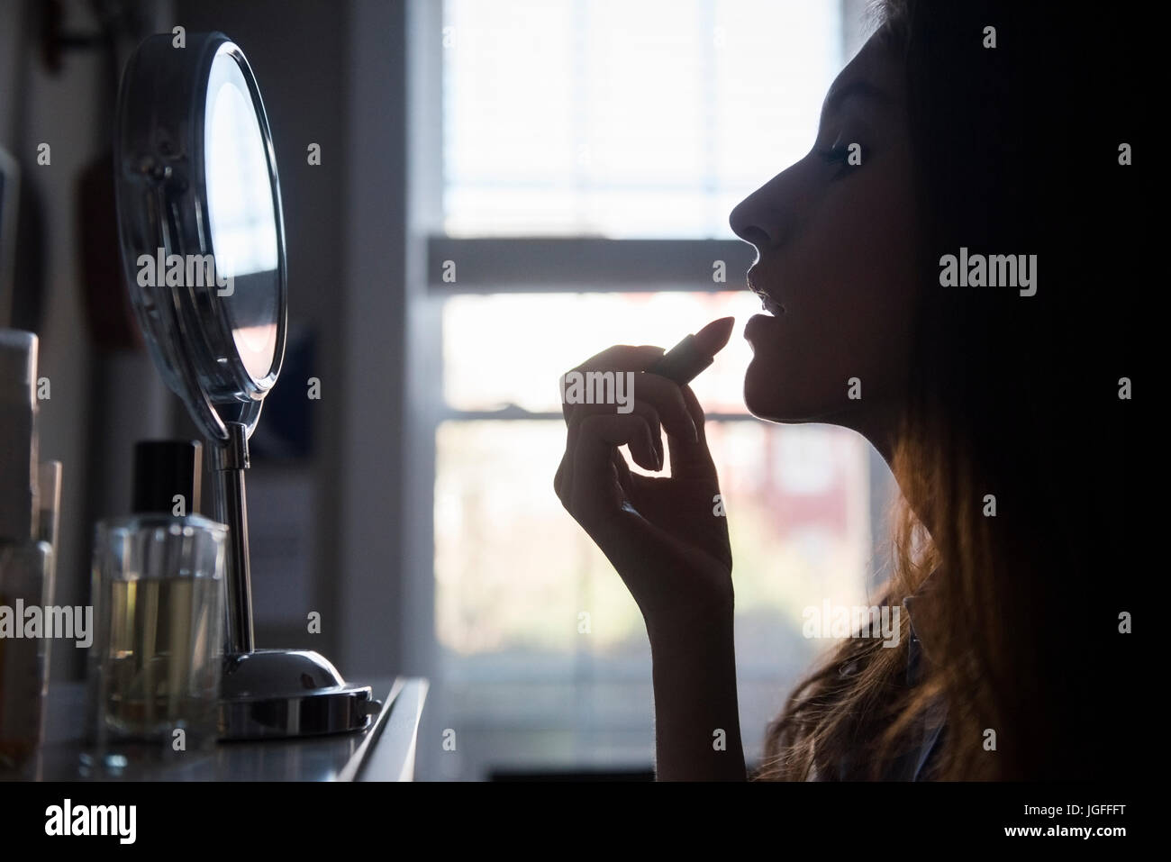 Silhouette of woman applying lipstick in mirror Stock Photo