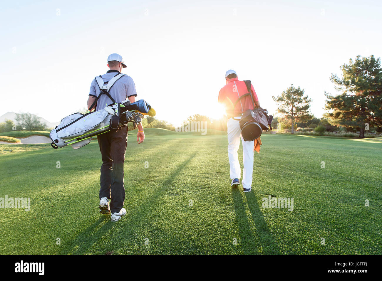 Men carrying golf bags on sunny golf course Stock Photo Alamy