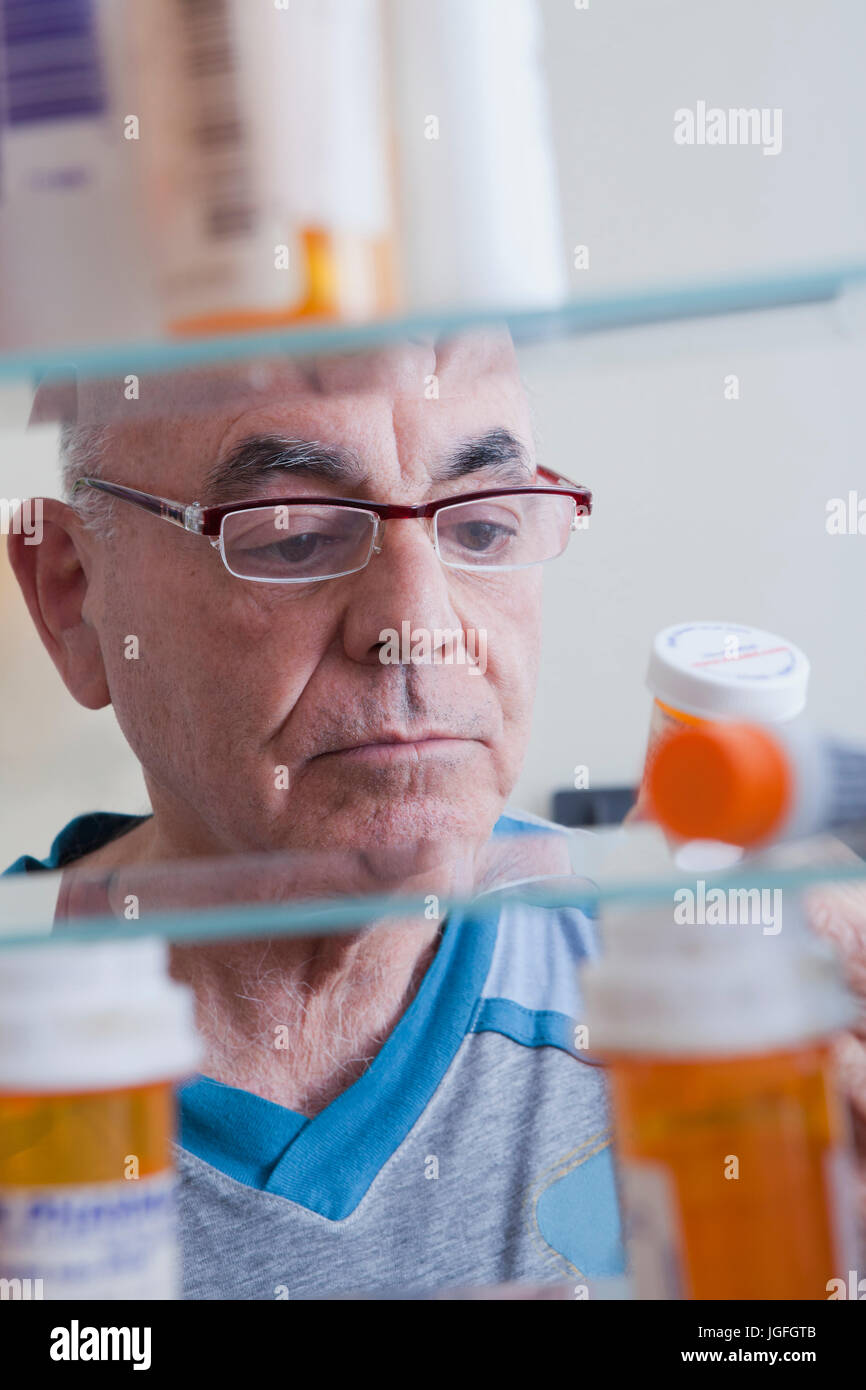 Hispanic man examining pill bottle from medicine cabinet Stock Photo