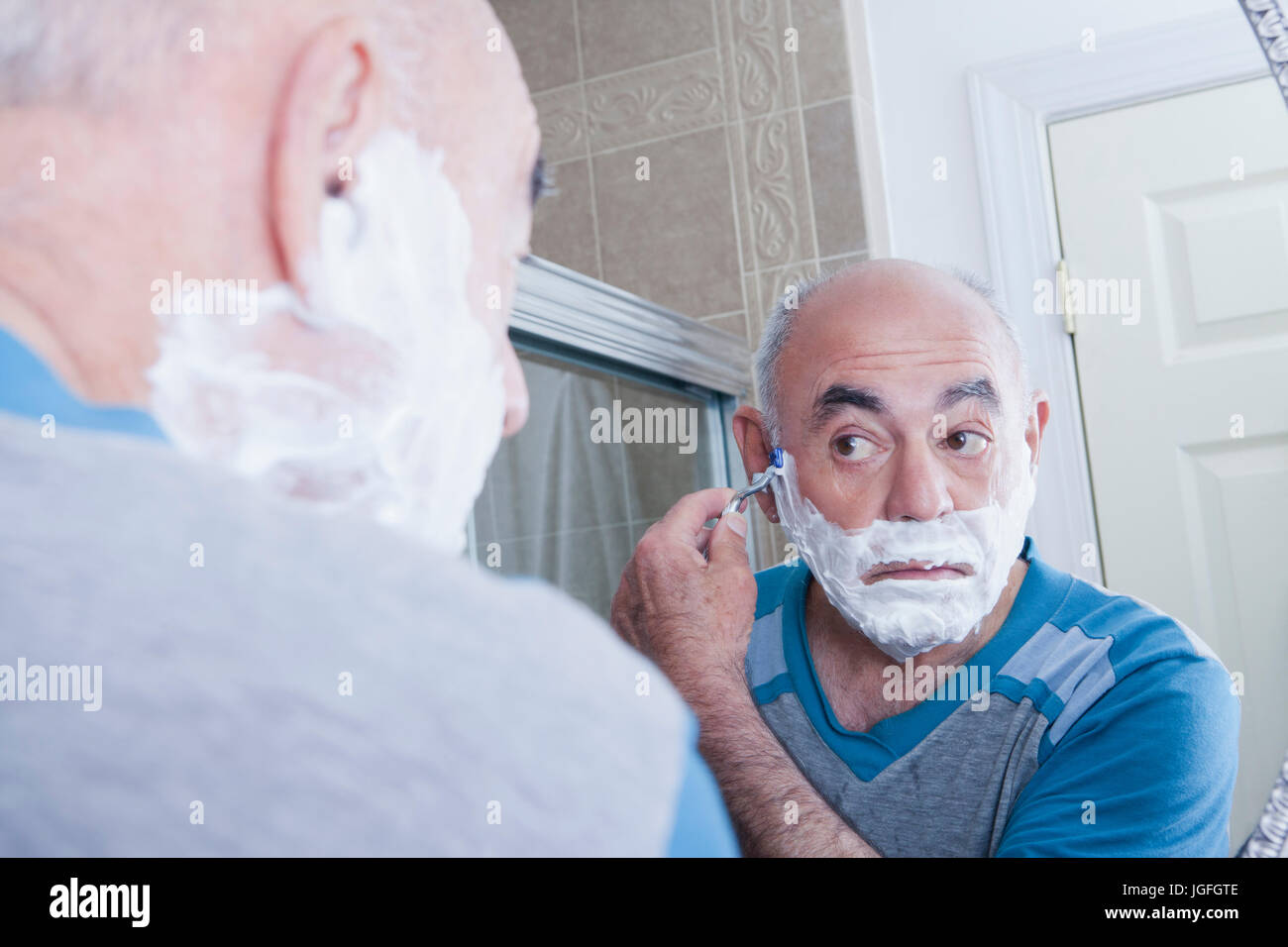 Reflection of Hispanic man shaving face in mirror Stock Photo