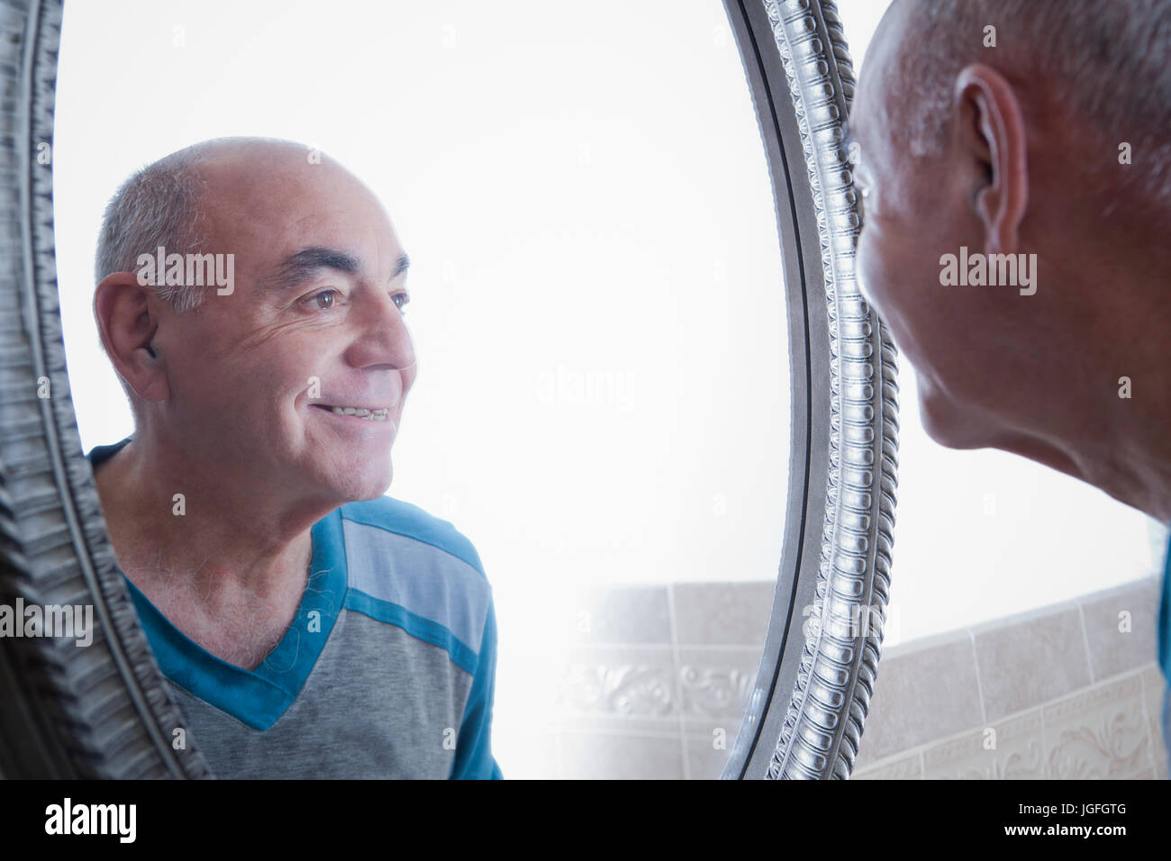 Reflection of smiling Hispanic man in bathroom mirror Stock Photo