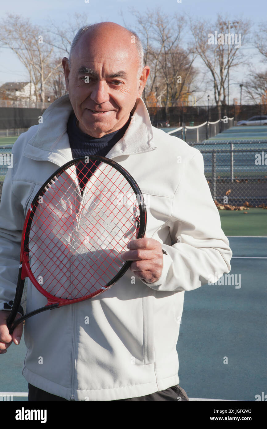 Smiling Hispanic man holding tennis racket Stock Photo