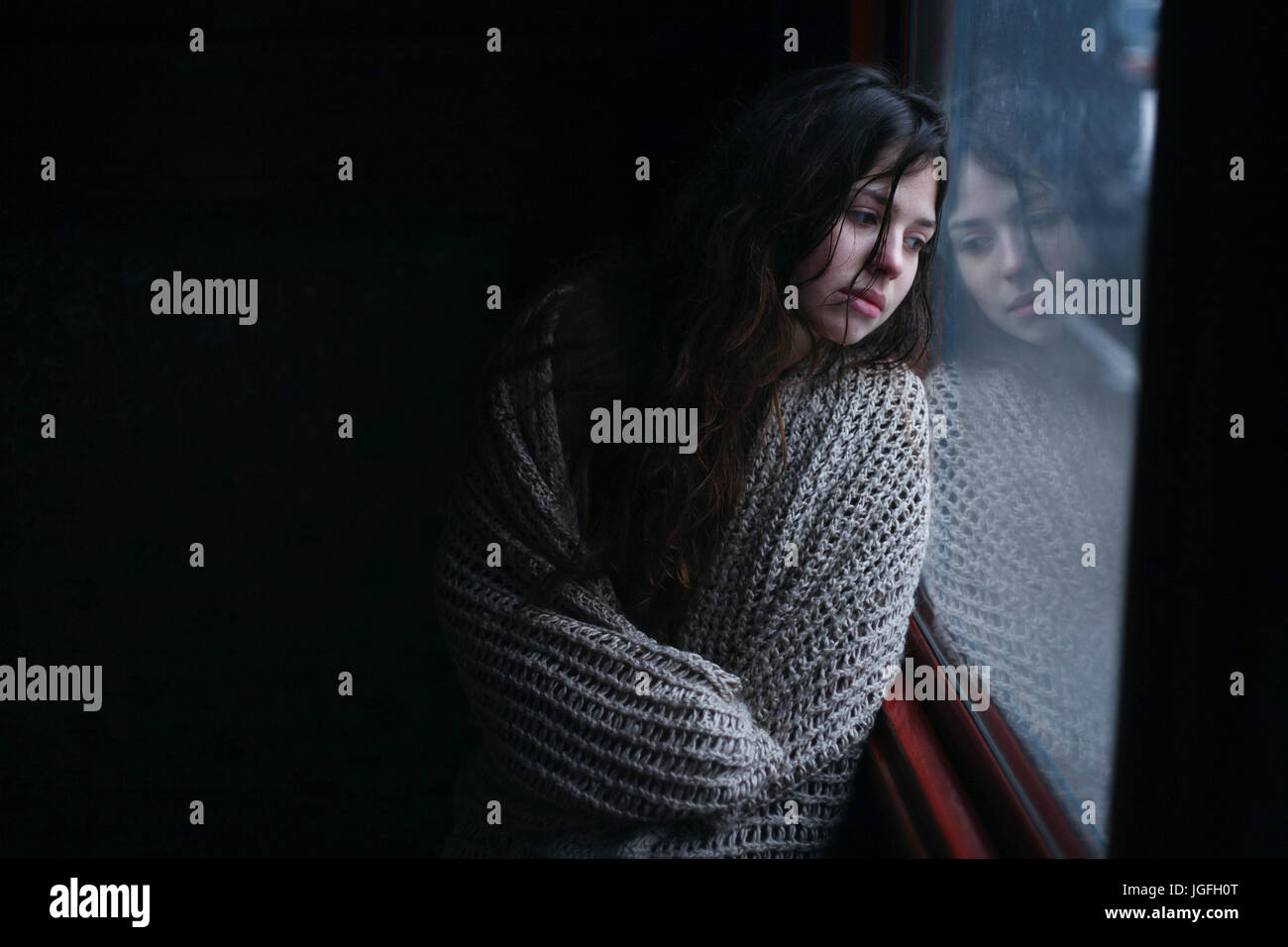 Sad Caucasian woman wrapped in scarf leaning on window Stock Photo