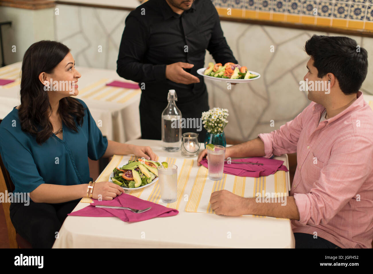 Waiter serving salad to Hispanic couple in restaurant Stock Photo