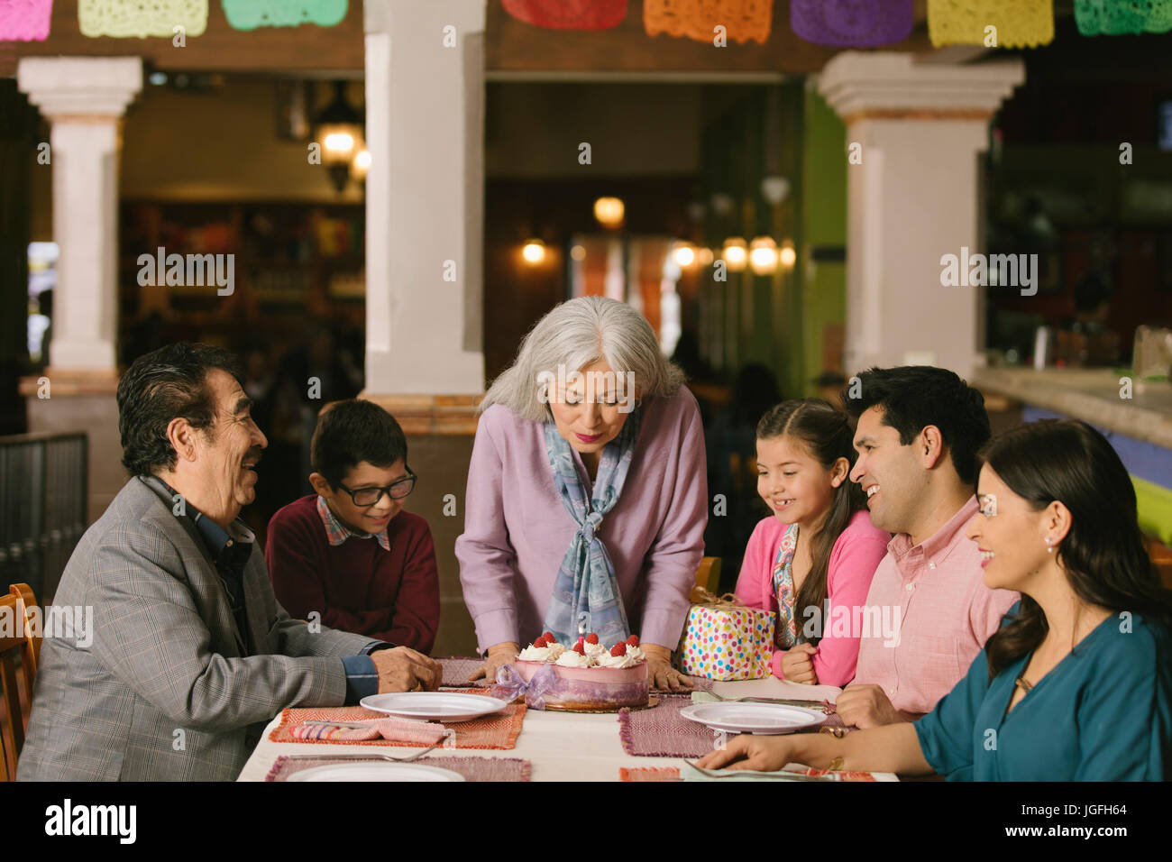 Older woman blowing out candles on birthday cake in restaurant Stock Photo