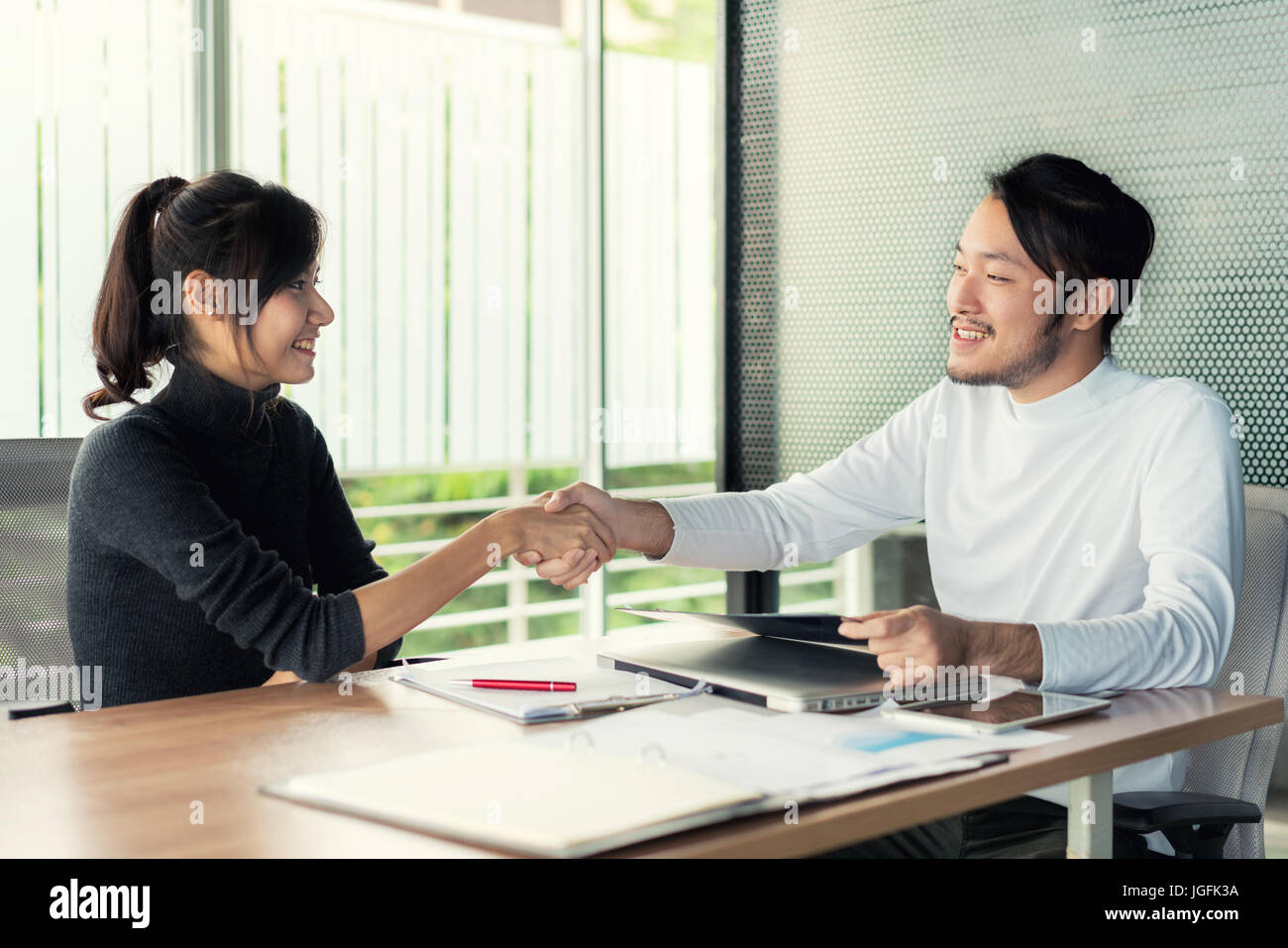 Couple of Asian business people with casual wear talking with happy and shaking hand in modern Office or coffee shop. Business sucess concept Stock Photo