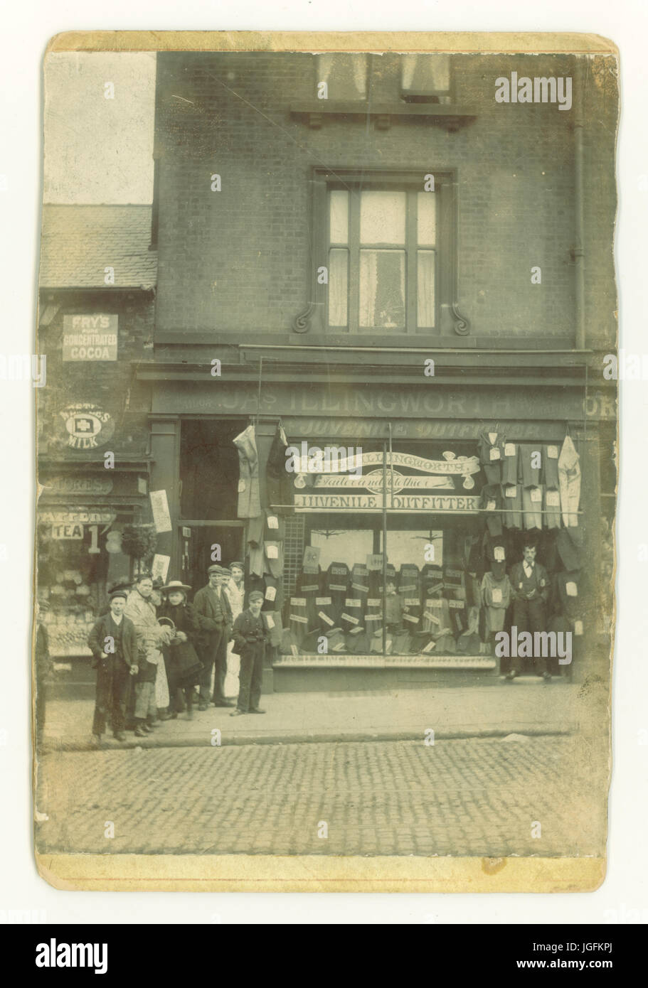 Edwardian photograph of J.A.S(James) Illingworth Juvenile Outfitters, Tailor and Clothier. 18 Attercliffe Road, Sheffield,South Yorkshire, England, U.K. Assistants / staff and customers from the grocery store next door have also posed for the photograph whilst the owner of the tailors maintains a dignified and humorless pose. Circa 1905. Stock Photo