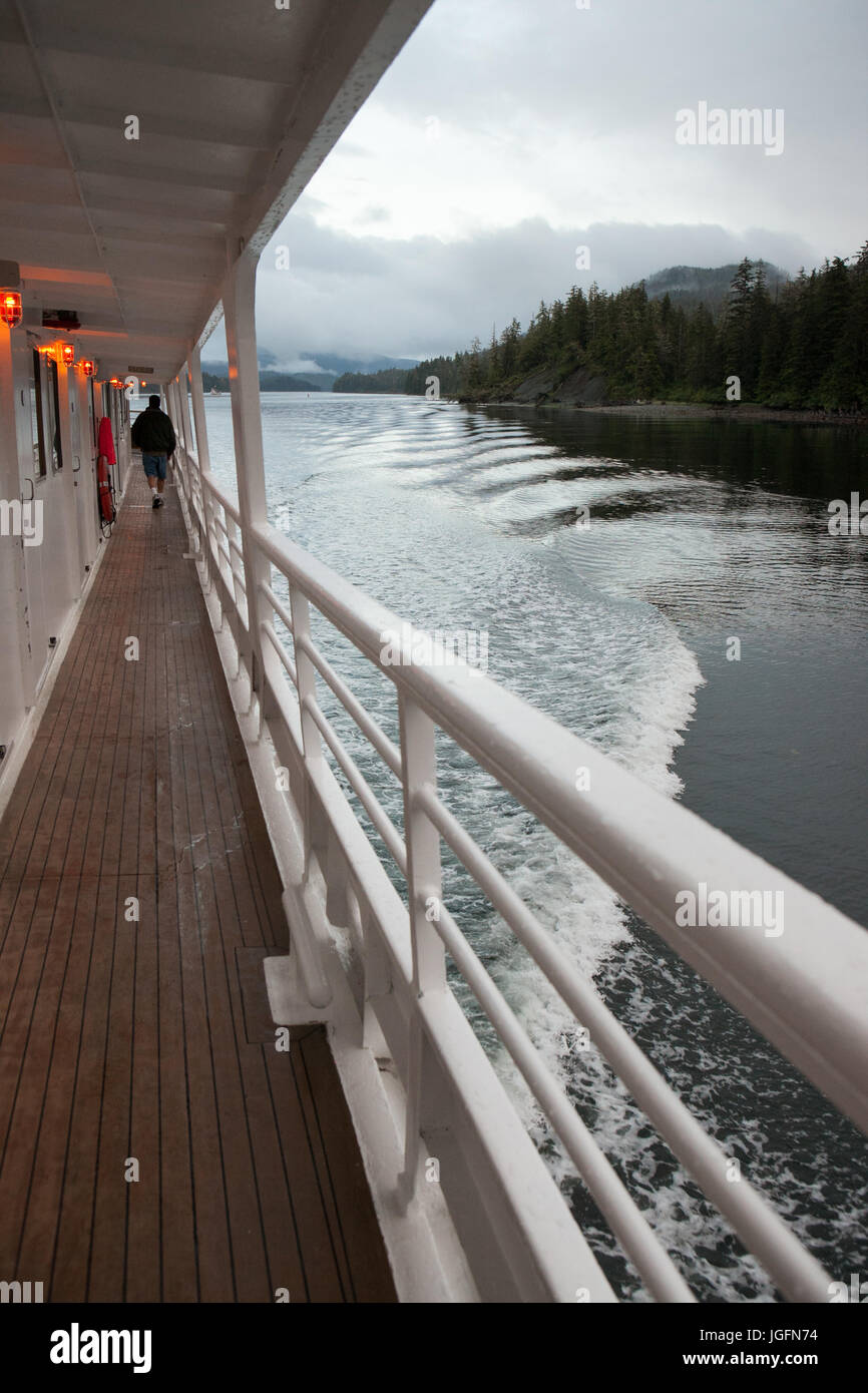 During an expedition on a cruise ship, a passenger walks near the railing along the outdoor corridor. Stock Photo