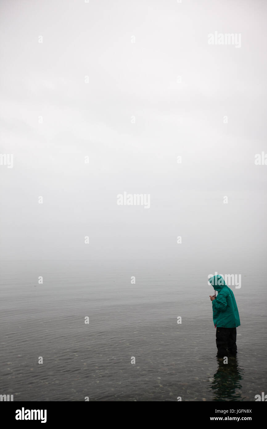 Amongst dense fog, a young girl stands in shallow water. Stock Photo